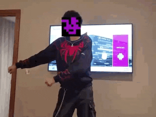 a man is dancing in front of a television while wearing a black sweater with a spider on it .