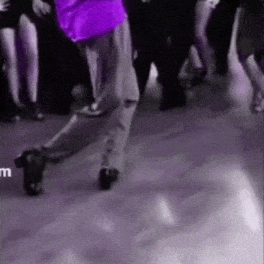 a man in a purple shirt is dancing in front of a crowd of people on a dance floor .
