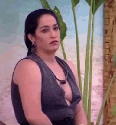 a woman in a very revealing top is sitting in front of a palm tree and looking at the camera .