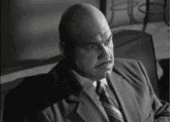 a bald man wearing a suit and tie is sitting in a chair