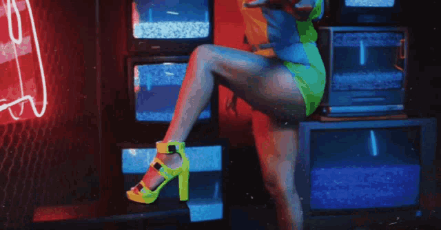 a woman in neon green heels is dancing in front of a stack of televisions