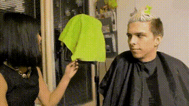 a man in a cape is getting his hair cut by a woman .