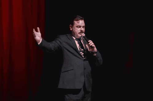a man in a suit and tie is speaking into a microphone on a stage