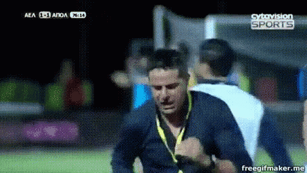 a man in a blue shirt with a yellow lanyard around his neck is running on a soccer field sponsored by sytovision sports