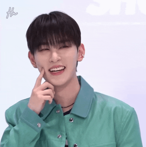 a young man wearing a green jacket is smiling with his hand on his chin