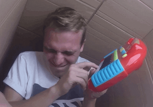 a man in a cardboard box is holding a red toy keyboard