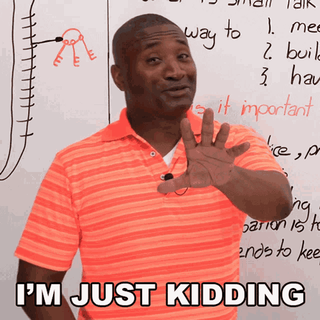 a man in an orange shirt says i 'm just kidding in front of a white board