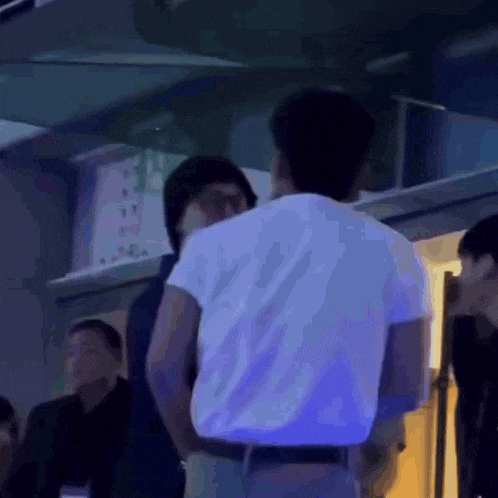 a man in a white shirt is standing next to another man in a dark room .
