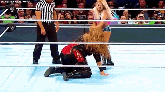 a woman is kneeling down in a wrestling ring while a referee stands behind her .