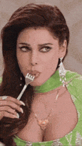 a woman in a green dress is holding a fork to her mouth .