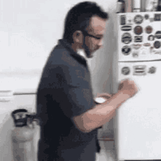 a man in a blue shirt is standing in front of a white refrigerator .