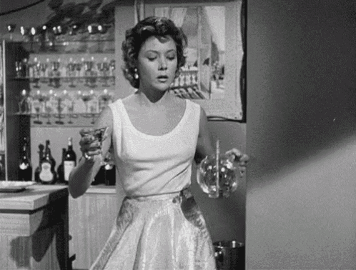 a woman in a white dress is standing in front of a bar holding a glass .