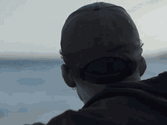 a man is wearing a baseball cap and looking out over the ocean .