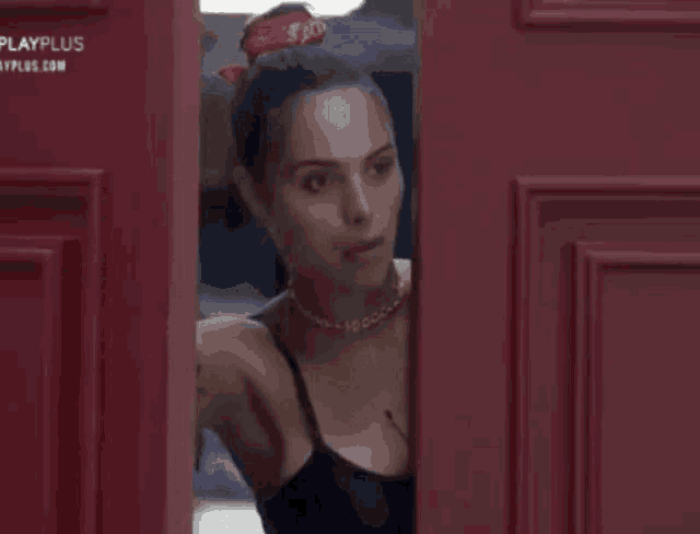 a woman in a black tank top is standing in a red doorway .