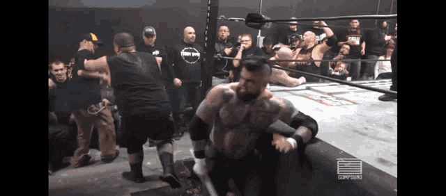 a group of men are watching a wrestling match and one of them is wearing a shirt that says " comm "