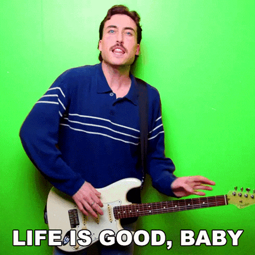 a man in a blue shirt is playing a guitar with the words life is good baby below him