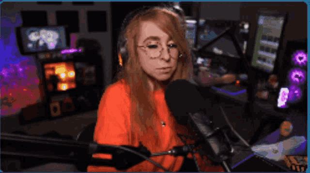 a woman wearing glasses and an orange shirt is sitting in front of a microphone in front of a computer