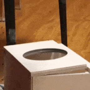 a white trash can with a hole in the middle is sitting on a wooden floor .