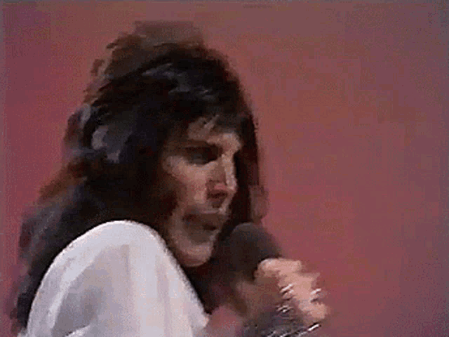 a woman singing into a microphone in front of a red wall