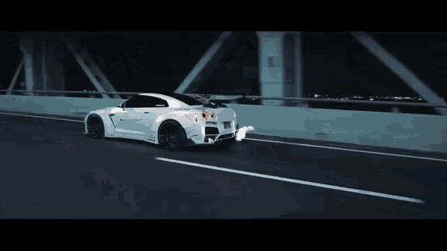 a white sports car is driving on a highway at night with flames coming out of the exhaust pipe .