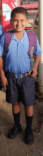a boy wearing a blue shirt and black shorts with a purple backpack on his back