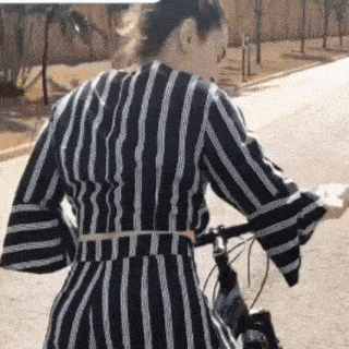 a woman in a striped dress is riding a bike down the street