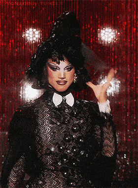 a drag queen is wearing a black dress and a black hat with a bow tie
