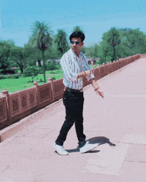 a man wearing sunglasses and a striped shirt walks on a sidewalk