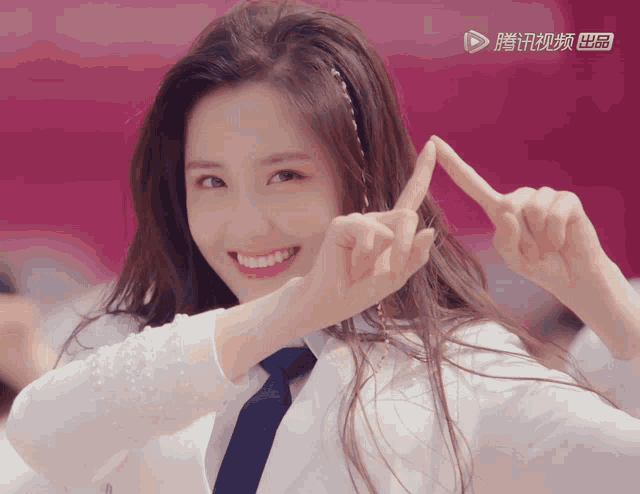 a woman making a heart shape with her fingers in front of a pink background with chinese characters on it