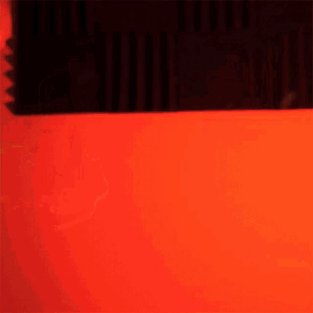 a silhouette of a person standing in front of a red wall with a flame coming out of it .