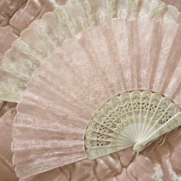 a pink and white fan is sitting on a pink blanket .