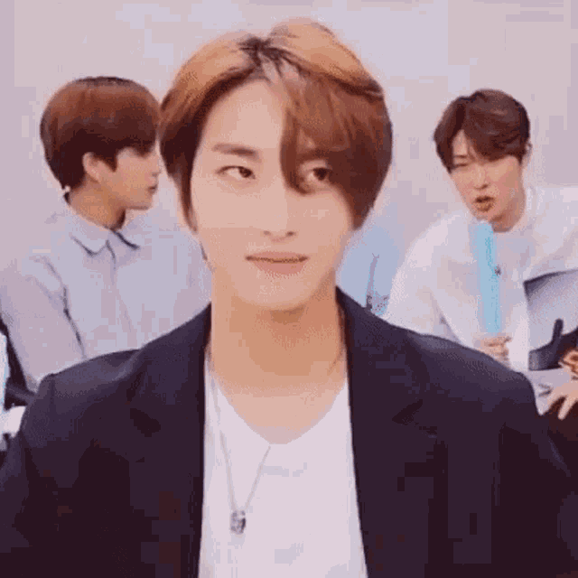 a young man in a suit is making a funny face while sitting in front of a group of people .
