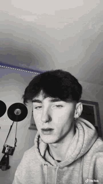 a young man in a grey hoodie is taking a selfie in a room .