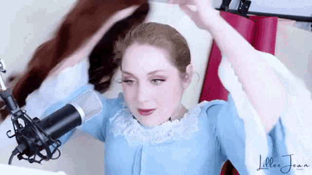 a woman in a blue dress is standing in front of a microphone with her hands in her hair .