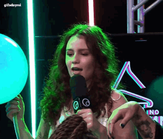 a woman is holding a balloon and talking into a microphone with a gifsdayrol logo behind her
