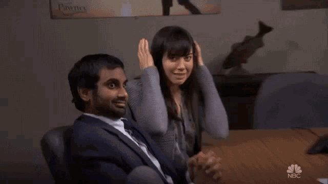 a man and a woman are sitting at a table and the woman is covering her face with her hands .