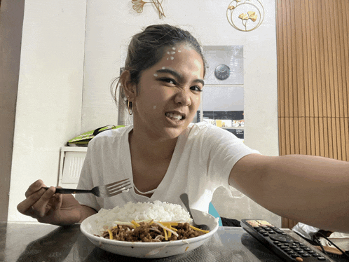a woman sitting at a table with a bowl of food and a remote