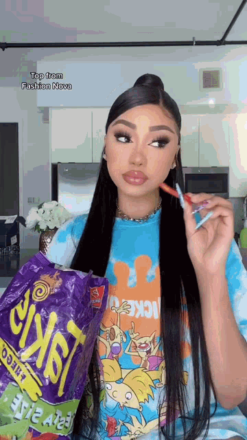 a woman in a nickelodeon t-shirt is holding a bag of fritos chips .