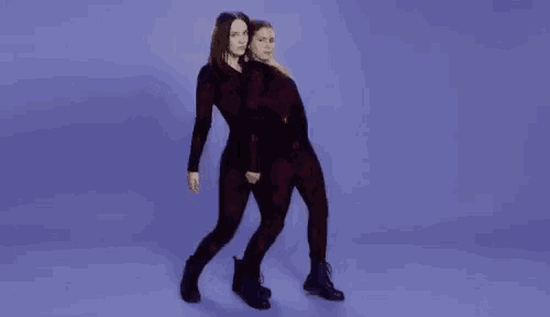 two women in red jumpsuits are dancing together in front of a purple background .