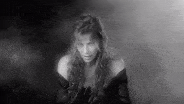 a black and white photo of a woman in a dark room with smoke coming out of her mouth .