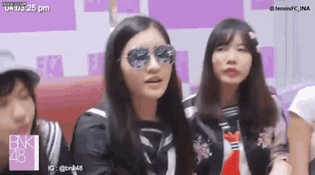 a group of girls are sitting in a room wearing sunglasses and a black shirt .
