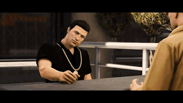 a man in a black shirt is sitting at a table with a gold chain around his neck
