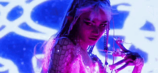 a woman with pink hair and dreadlocks is standing in front of a blue and purple light .