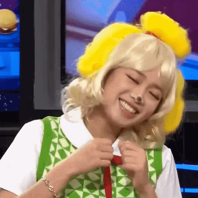 a woman is wearing a yellow wig and smiling while sitting in front of a television .