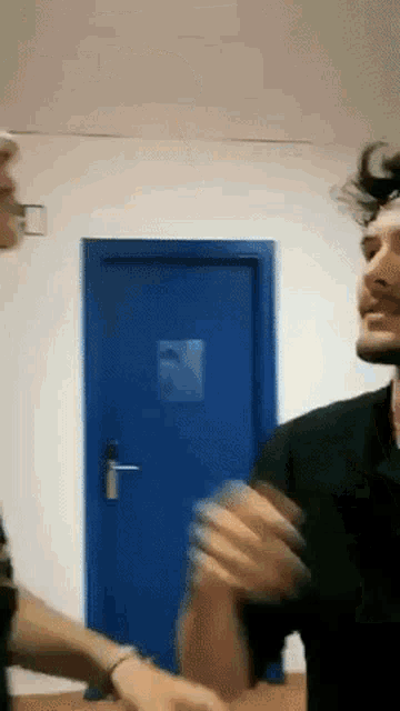 a man standing in front of a blue door talking to another man