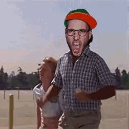 a man wearing glasses and an orange hat is running with a woman behind him