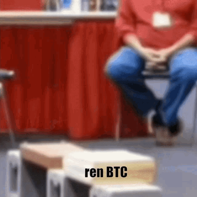 a blurry picture of a man sitting in a chair with the words ren btc on the bottom right