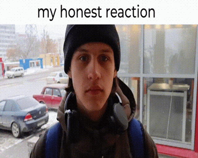 a man wearing headphones and a beanie is standing in front of a building with the words " my honest reaction " above him