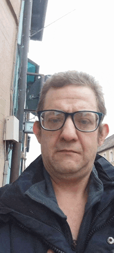 a man wearing glasses and a jacket is standing in front of a sign that says ' a ' on it