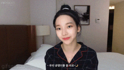 a girl in a plaid shirt is sitting on a bed with a picture on the wall above her that says aespa